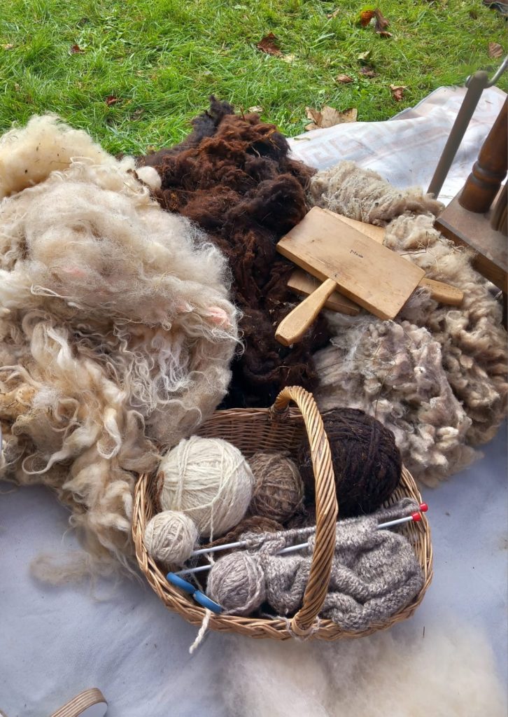 Fibre, balls on yarn, a work in progress and tools used in working with wool on a blanket on the ground
